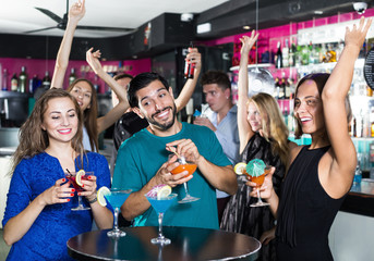 Smiling man with two women are drinking cocktails