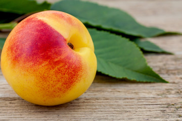 Peach fruit with leaves on rustic wood, yellow ripe nectarine