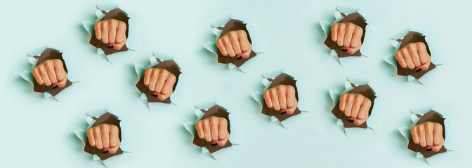 Chaotic pattern of female fists punching through blue paper background. War, struggle, conflict, feminist concept. Banner with copy space - obrazy, fototapety, plakaty