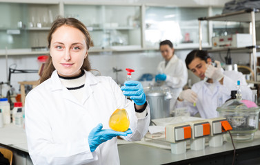 Female chemist analyzing liquid in test flasks