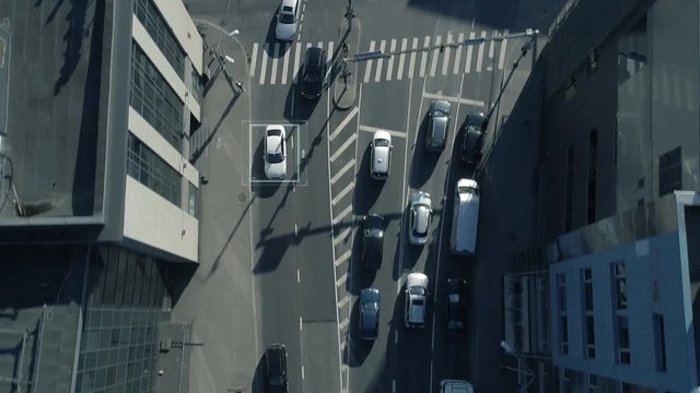 Top Down Aerial Drone Tracking Shot: White Autonomous Self Driving Car Moving Through City. Concept: Artificial Intelligence Scans Surrounding Environment, Detecting Cars, Avoids Traffic Jams.