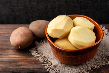 Raw peeled potatoes in bowl on dark wooden background.