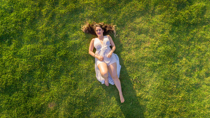 Aerial view. Young girl lying and resting on lawn on sunny day in park on grass. Above view. Woman on grass in meadow.