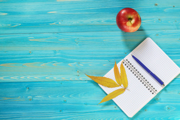 Notebook for records, Apple and autumn leaves on a wooden table