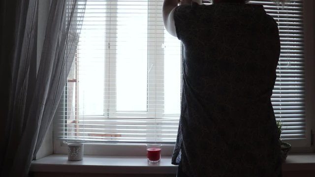 A woman silhouette opens blinds jalousie in the morning at home