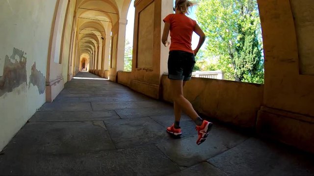 SLOW MOTION: A sportwear woman running under San Luca's portico: the longest porch in the world leading to the San Luca Sanctuary on Colle della Guardia hill. Bologna city of Italy.