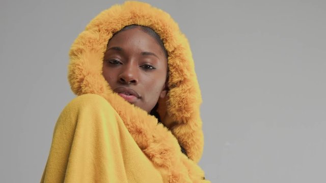 black mixed race woman poses to the camera wears yellow outwear poncho with fur