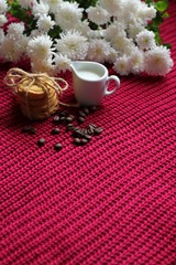 Coffee beans with milk, pile of delicious chip cookies tied with twine and white flowers on a red knitted background. Good morning concept. Enjoy slow life