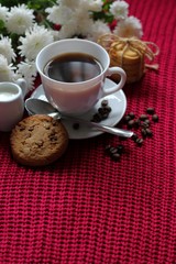 Traditional continental breakfast, cup of coffee espresso with milk, pile of delicious chip cookies tied with twine and white flowers on a red knitted background. Good morning concept. Enjoy slow life