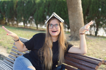 Blonde girl with glasses with a book on her head having fun outdoor