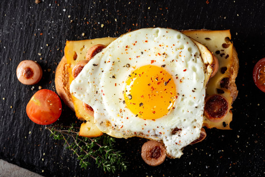 Open sandwich made with egg, cheese and sausages on a dark slate