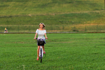 Soft focus photo. A young, beautiful blond woman with a white bike in a green meadow.