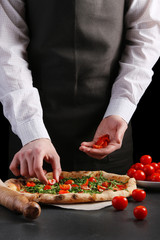 Chef puts cherry tomatoes in pizza preparation of traditional Italian pizza. cooking pizza concept. pizza making on black background