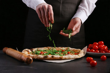 The chef in black apron makes pizza with vegetables