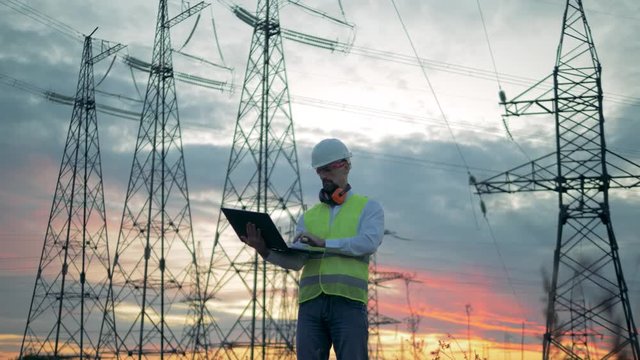 Power lines constructions and a male engineer operating a laptop