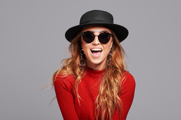 Fashion portrait pretty woman in black rock style hat and sunglasses over grey background. Holiday...