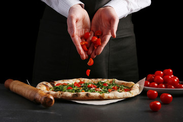 chef making pizza on dark back. chef's hand sprinkles cherry tomatoes in pizza