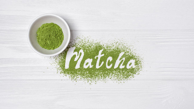 Lettering from green matcha tea on white wooden background