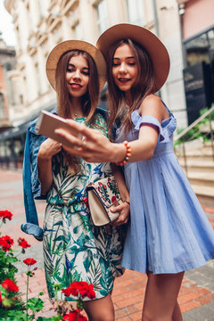 Outdoor portrait of two young beautiful women taking selfie using phone. Girls having fun in city. Best friends
