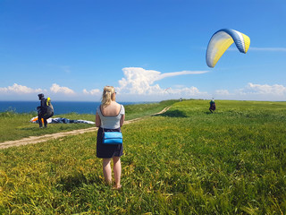 Woman watching adult paraglider near cliff along baltic sea coastline and green meadow wheat field...