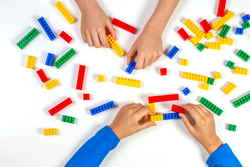 Kids hands playing with colorful building plastic bricks on white background. Educational developing toys background