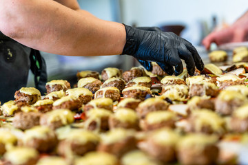 Female Chef Putting Ingredients of Burgers on a Sliced Bread Spread on a Table in Black Gloves - Concept of the Hard Working Person and the Hygiene in the Kitchen