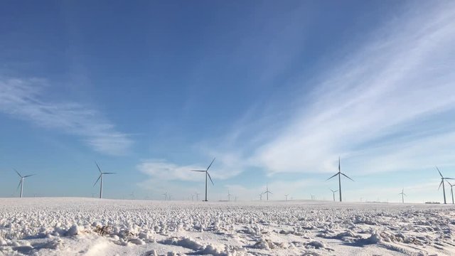 Wind energy farm in snowy field in ND with propellers spinning from wind together on beautiful sunny day.
