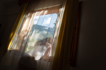 In sunny morning, from window of a room, romantic mountain view behind the curtains. The girl...