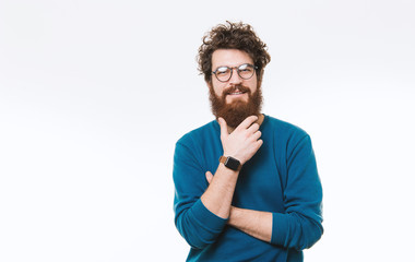 Bearded hispter guy in glasses is posing and looking at camera over white background