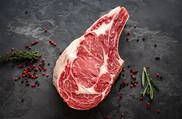 Foto op Plexiglas raw cowboy steak with seasonings on stone background, prime rib eye on bone, top view © Andrey