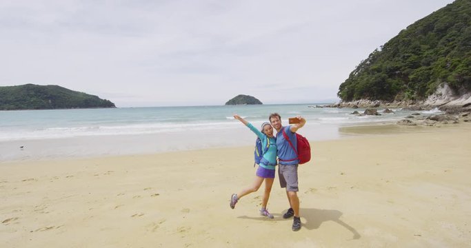 Couple on travel having fun taking selfie phone video on travel vacation backpacking on beach. People on Abel Tasman Coast Track, one of the Great Walks and tramping tracks of New Zealand. SLOW MOTION