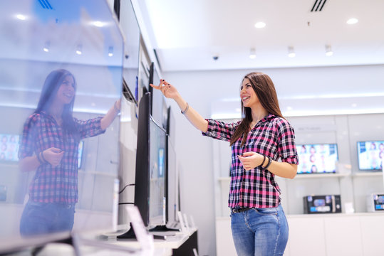 Happy Caucasian brunette with long hair choosing television while standing in tech store.