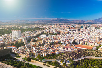 Fototapeta na wymiar Panoramic view of the city of Alicante, Spain. Block of apartment buildings, parks, roads, houses, palm trees and bullring against the background of a mountain landscape in the blue sky