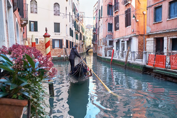 Venice, Italy - February 10, 2018: Gondolier rides gondola through the narrow canal between...
