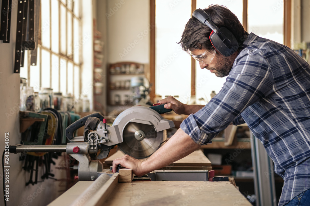 Wall mural Carpenter sawing wood with a mitre saw in his workshop