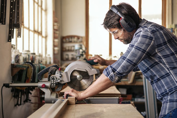 Carpenter sawing wood with a mitre saw in his workshop