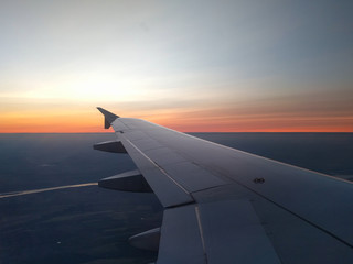 Plakat View from airplane window to beautiful sunrise or sunset. Wing of plane flying above in the sky.