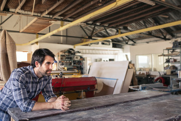 Woodworker leaning on a workshop bench deep in thought