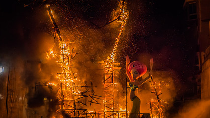 Left figure of an eastern woman in front of the burning structure of the burning Falla Taut during la Crema final event during Las Fallas festival in Valencia Community in Spain.