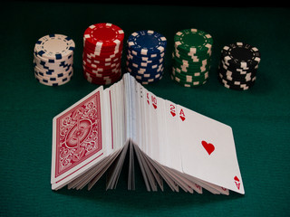 A deck of poker cards and poker chips of various colors on a green mat