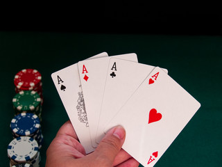 A person playing poker with the four aces of a deck in his hand and poker chips of various colors on a green mat