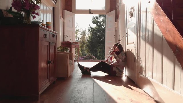 Hispanic Woman Practices Violin Seated On The Floor Of A Hallway Inside A Beautiful House. 4k