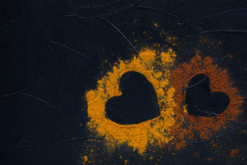 Two hearts from spices curry powder and pepper cayenne on dark background. St. Valentine's day...