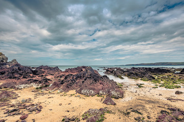 Rocky beach and moody sky over sea horizon on Pembrokeshire coast,Uk.Red rock formation on diverse shoreline.Nature image with copy space.