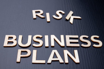 The inscription is arranged from letters cut out of wood on the table. The word business plan, risk.