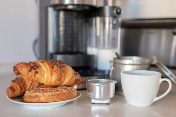 Freshly brewed coffee from a coffee machine and a tasty sweet croissant. Breakfast in the home kitchen.