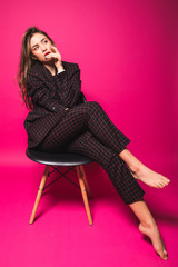 Fashionable young woman sitting on chair on pink background