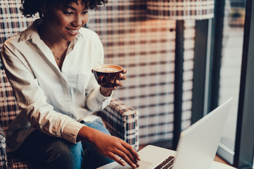 Lady with cup of coffee looking at laptop and smiling
