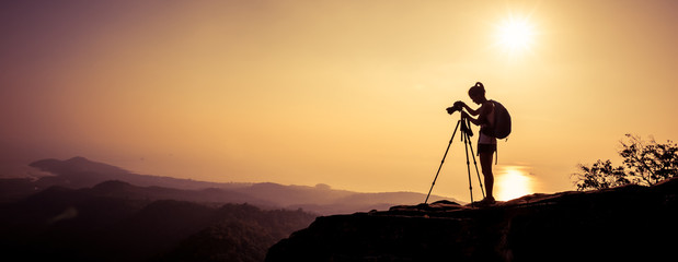 woman photographer taking photo on sunset mountain peak - obrazy, fototapety, plakaty