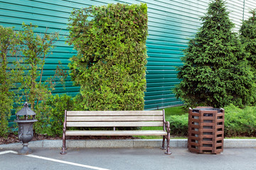 wooden bench with iron forged legs near an urn in the background, green plants and a fence.